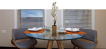 A glass table with two cushioned chairs in front of windows